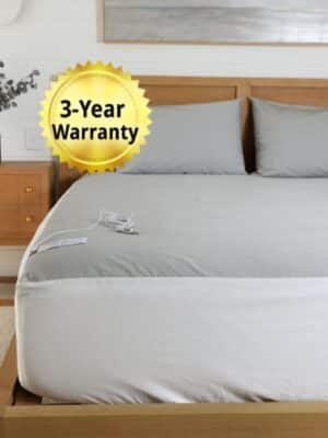 Grounding sheet fully fitted on a bed with cord and EarthShield tag visible, shown in a natural bedroom setting to show setup and use of the indoor earthing products.