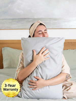 Person sitting on a bed, hugging a grounding pillowcase with cord connected, showing comfort and use of the EarthShield Grounding Pillowcase.